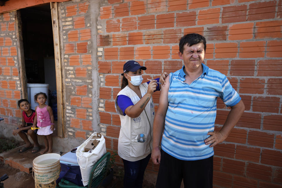 Healthcare worker Lorena Aranda gives Elvio Rojas a shot of the Pfizer COVID-19 vaccine as his children watch from their home during a door-to-door vaccination campaign in Luque, Paraguay, Monday, Jan. 24, 2022. (AP Photo/Jorge Saenz)