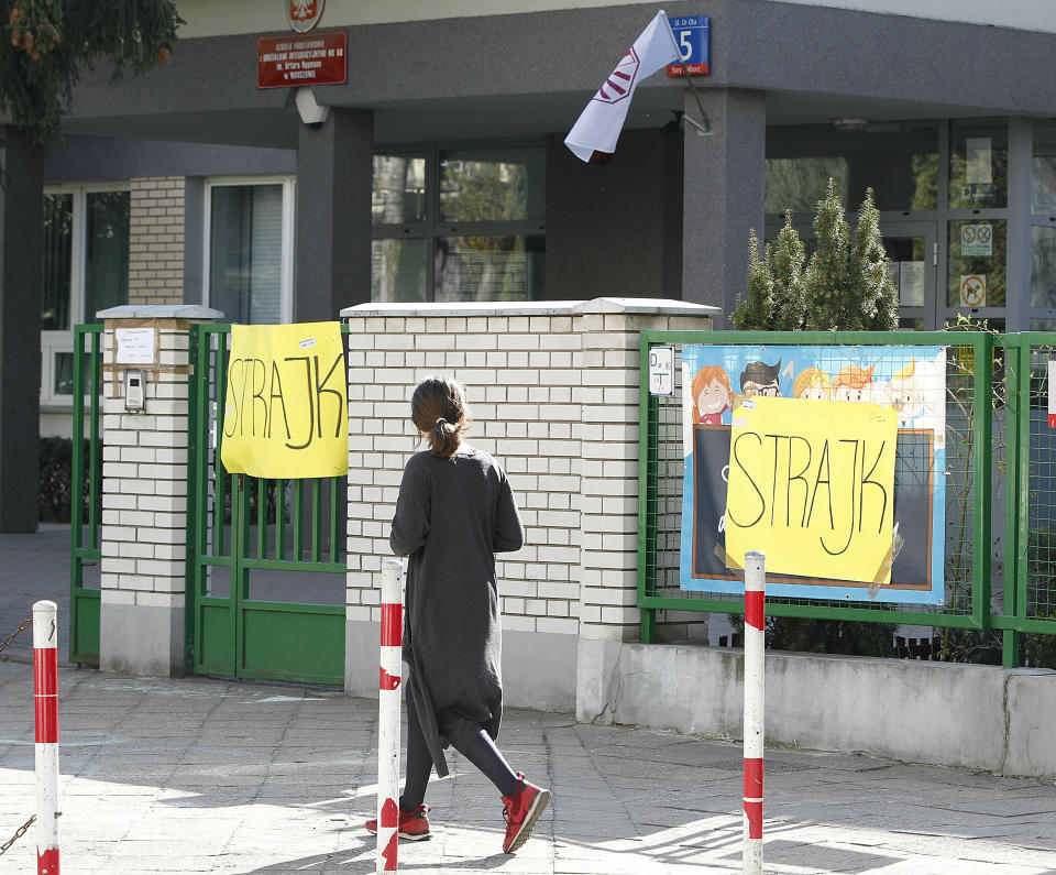 A woman walks by a school where teachers are taking part in nationwide pay strike, with banners declaring the participation in the strike and also parent's support for it, in Warsaw, Poland, Monday, April 15, 2019. The right-wing government says it has money only to grant half of the teachers' demands in a sign that its policy of pre-election spending has reached its limit.(AP Photo/Czarek Sokolowski)