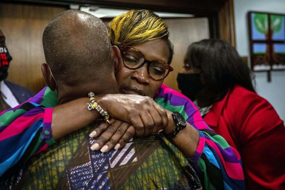 A Black woman wearing glasses embraces a man facing away from the camera.