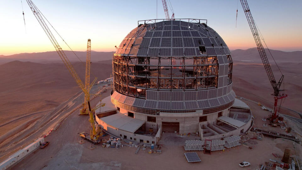  A giant domed building under construction on the top of a desert mountain. 