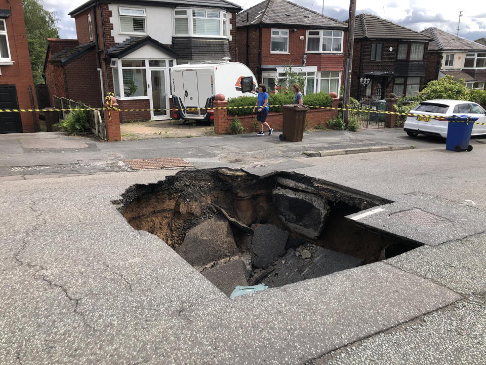 A huge sinkhole has suddenly appeared in the middle of a busy road - leaving homeowners fuming.  See SWNS story SWLShole.  The ground gave way to the massive chamber, measuring roughly six feet deep and ten feet wide, today (Mon) on Heywood Road, Prestwich, Grtr. Manchester.  Traffic was brought to a standstill following the shocking incident, with a hasty perimeter set up around it by police and locals.  But locals who gathered at the chasm vented their anger at the poor quality of the road running past their properties, where most are valued at around £300,000. 