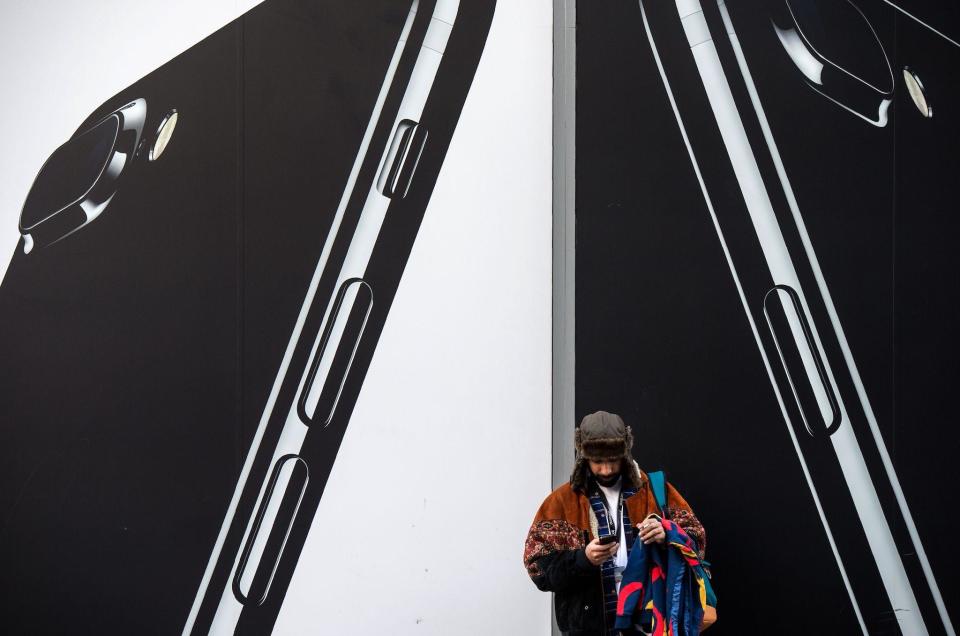 A man checks his phone next to billboards advertising the an Apple iPhone 7 smartphone as he stands on Oxford Street in London on March 7, 2017: CHRIS J RATCLIFFE/AFP via Getty Images)