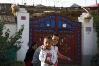 In this Sept. 20, 2018, photo, Uighur children play while their relatives rest outside their house, decorated with Chinese lanterns and barbed wire at the Unity New Village in Hotan, in western China's Xinjiang region. While thousands of Uighur Muslims across China’s Xinjiang region are forced into re-education camps, China’s fledgling vision for ethnic unity is taking shape in a village where Han Chinese work and live alongside Uighur minorities. (AP Photo/Andy Wong)