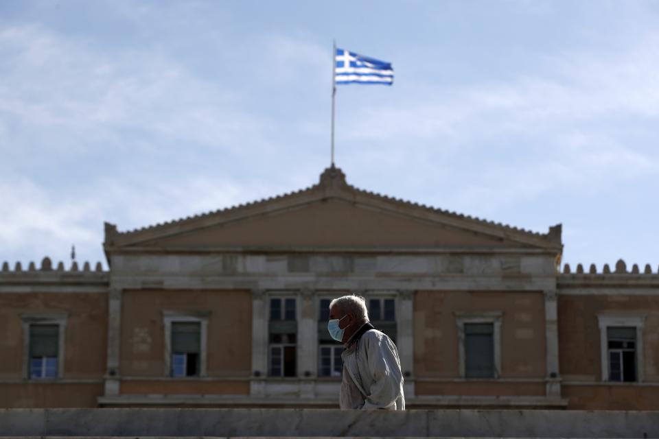 A pedestrian wearing a face mask to curb the spread of COVID-19 walks in front of the Greek parliament in central Athens, Tuesday, Oct. 20, 2020. Greece has been experiencing a resurgence of the virus, with the number of new daily cases, most in the Greek capital, often topping 400, and both deaths and the number of those in intensive care units rising. (AP Photo/Thanassis Stavrakis)