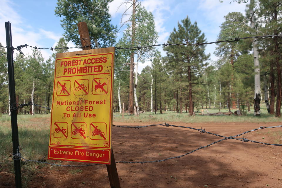 A sign warning of the closure of the national forest surrounding Flagstaff, Ariz., hangs on barbed wire fence on Wednesday June 23, 2021. The Coconino National Forest is one of a handful of forests in Arizona that closed this week amid high fire danger and as resources are stretched thin with blazes burning across the state. (AP Photo/Felicia Fonseca)