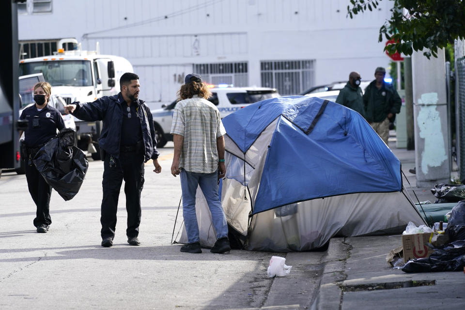 FILE - A City of Miami police officer talks with a homeless person, prior to a cleaning of the street, Tuesday, Nov. 16, 2021, in Miami. Florida’s homeless will be banned from sleeping in public spaces such as sidewalks and parks under a law signed Wednesday, March 20, 2024, by Republican Gov. Ron DeSantis. (AP Photo/Lynne Sladky, File)