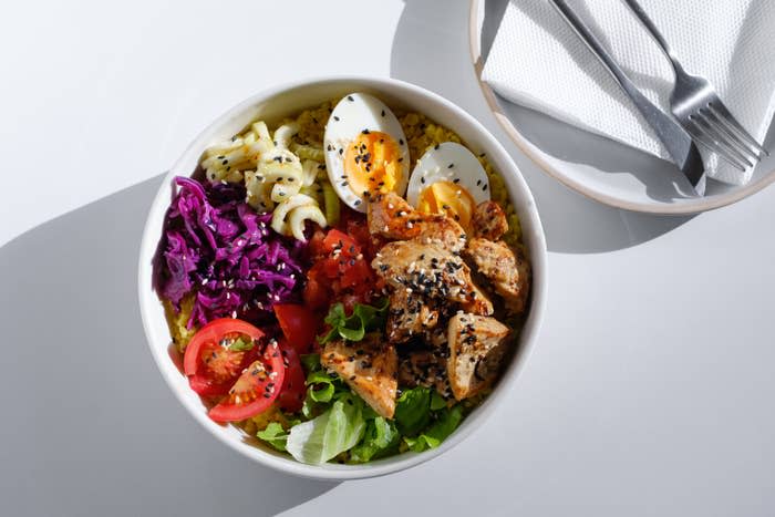 Bowl of salad with grilled chicken, boiled eggs, sliced tomatoes, purple cabbage, and greens, garnished with sesame seeds