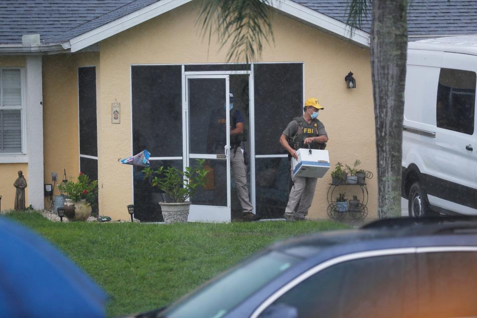 An FBI agent walks out of the door of the house with a box