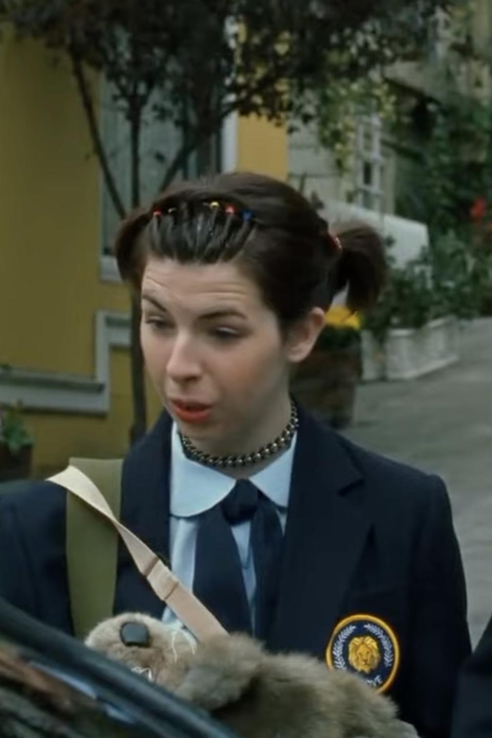 A person in a school uniform with pigtails and a choker necklace stands next to a person with short hair, looking at something in front of them