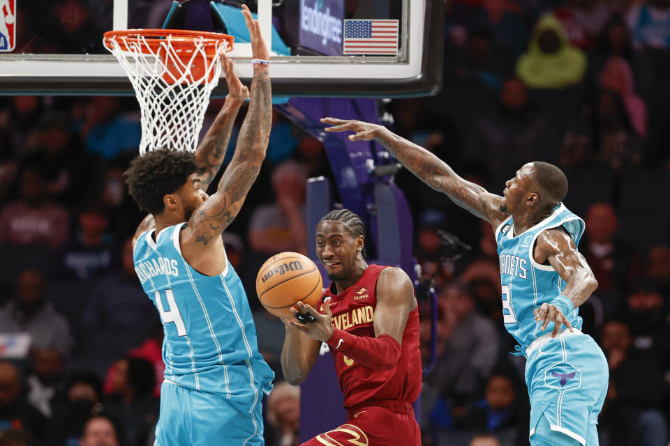 Cleveland Cavaliers guard Caris LeVert, center, passes between Charlotte Hornets center Nick Richards (4) and guard Terry Rozier during the first half of an NBA basketball game in Charlotte, N.C., Sunday, March 12, 2023. (AP Photo/Nell Redmond)