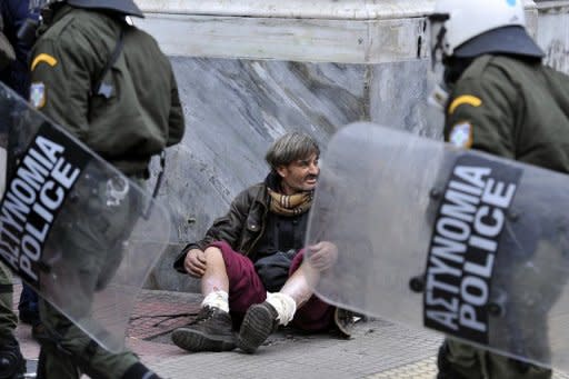 A beggar looks at passing riot police during a protest rally in Athens. Greece's cabinet Saturday approved tough austerity measures demanded by EU and IMF creditors after the prime minister warned that a failed debt deal and default would spark "uncontrolled chaos"