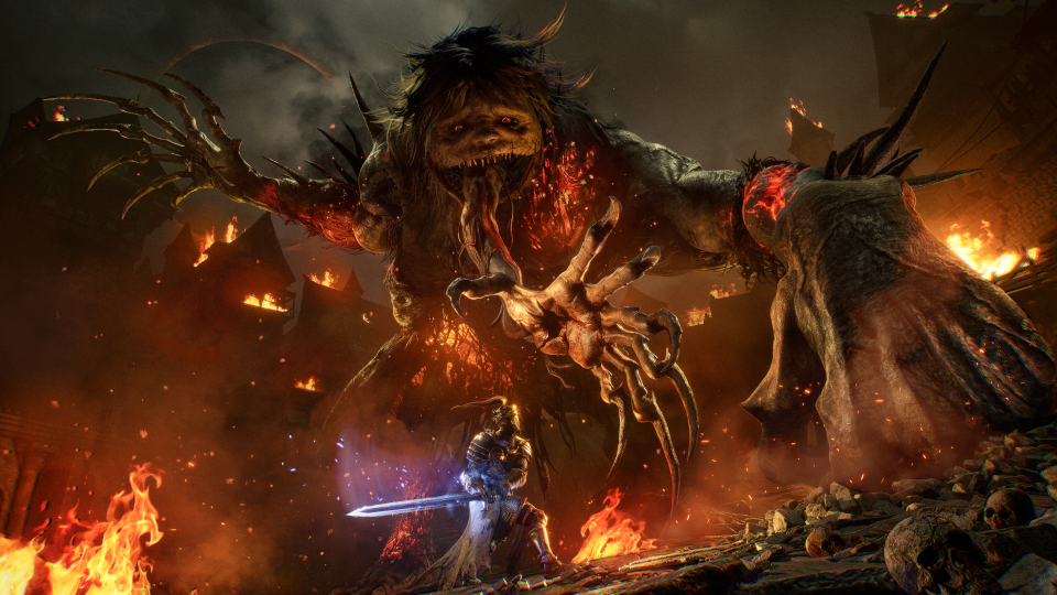  The Spurned Progeny from Lords of the Fallen looms horrifically over a player amidst burning rubble, a clawed hand tearing from its maw to snatch them up. 