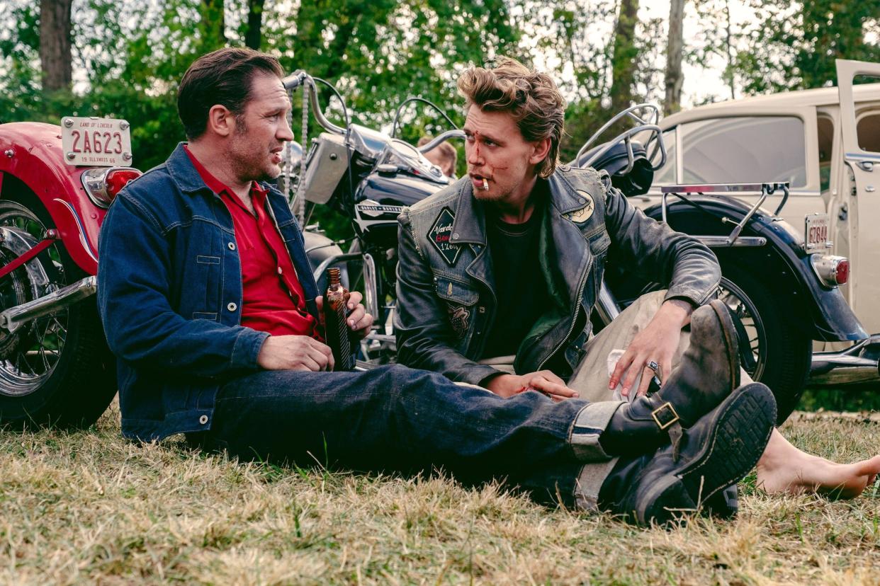 Tom Hardy and Austin Butler sat on the grass in a scene from The Bikeriders