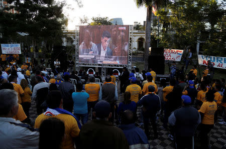 People watch on a giant TV screen congress members participate in a discussion on a proposed amendment to allow presidential second terms, during a session at the Lower House of Congress in Asuncion, Paraguay April 26, 2017. REUTERS/Jorge Adorno