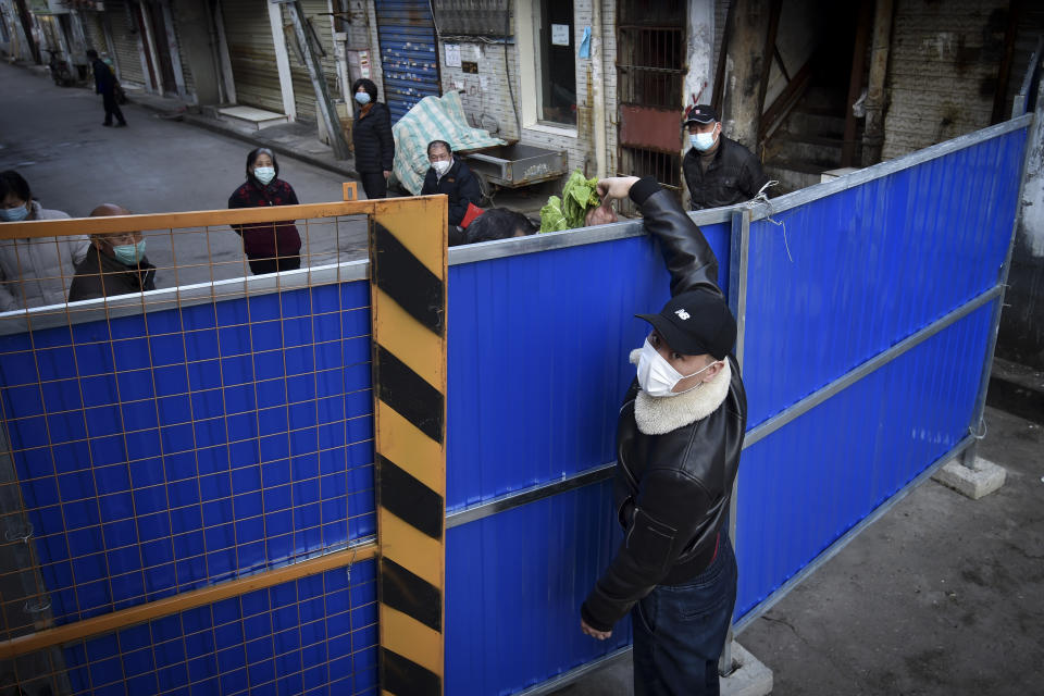 FILE - In this Feb. 23, 2020, file photo, a man wearing a protective face mask passes groceries through the barricades blocking a residential area in Wuhan in central China's Hubei province Sunday. A 10-member team of international researchers from the World Health Organization hopes to find clues as to the origin of the coronavirus pandemic in the central Chinese city of Wuhan where the virus was first detected in late 2019. (Chinatopix via AP, File)