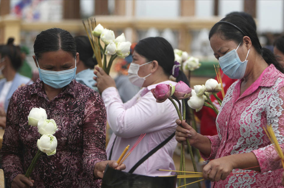 Buddhist followers wearing face masks hold incense sticks and lotus flowers to offer for prayer in front of Royal Palace during Buddhist holidays in Phnom Penh, Cambodia, Friday, Sept. 25, 2020. (AP Photo/Heng Sinith)