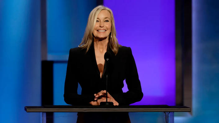 Bo Derek wearing black and smiling while standing in front of a podium