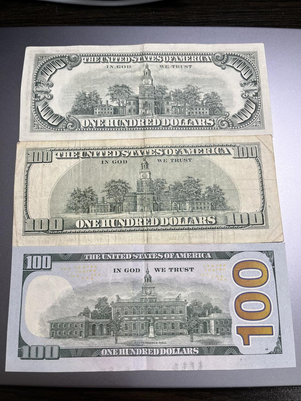 Back view of all three: 1977 has an ornate font for "100," 2003 has a simpler font, 2017 has a new illustration of Independence Hall and a redesigned, large vertical "100" in a different font