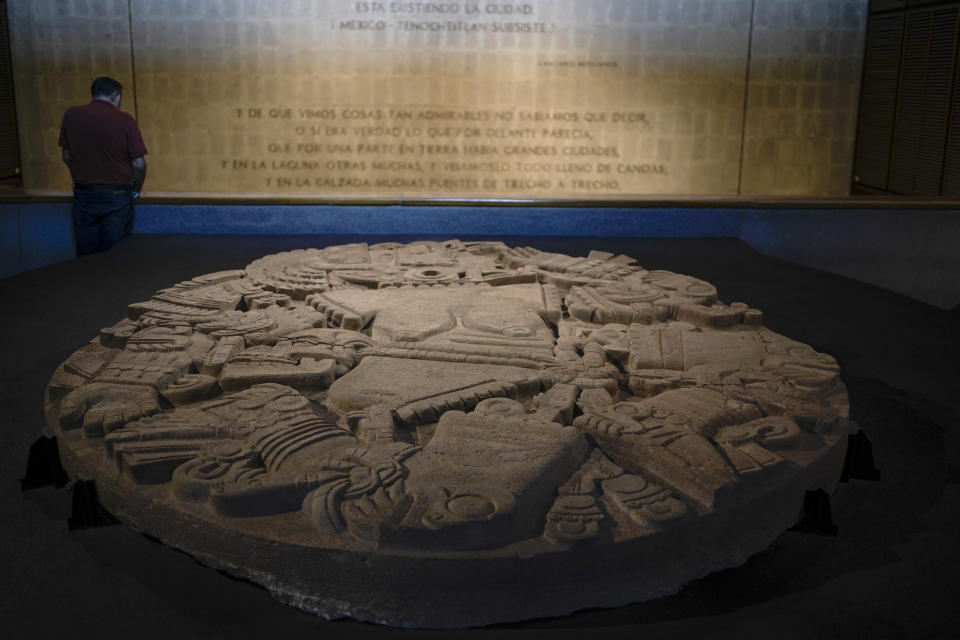 A visitor reads information displayed on a wall while standing next to a monolith depicting the Mexica lunar goddess Coyolxauhqui, at the Museum of Templo Mayor, marking the 45th anniversary of the circular stone’s discovery, in Mexico City, Wednesday, March 29, 2023. The finding was a milestone for Mexican archaeology, as it shed light on Mexica civilization before the Spanish conquest. (AP Photo/Eduardo Verdugo)