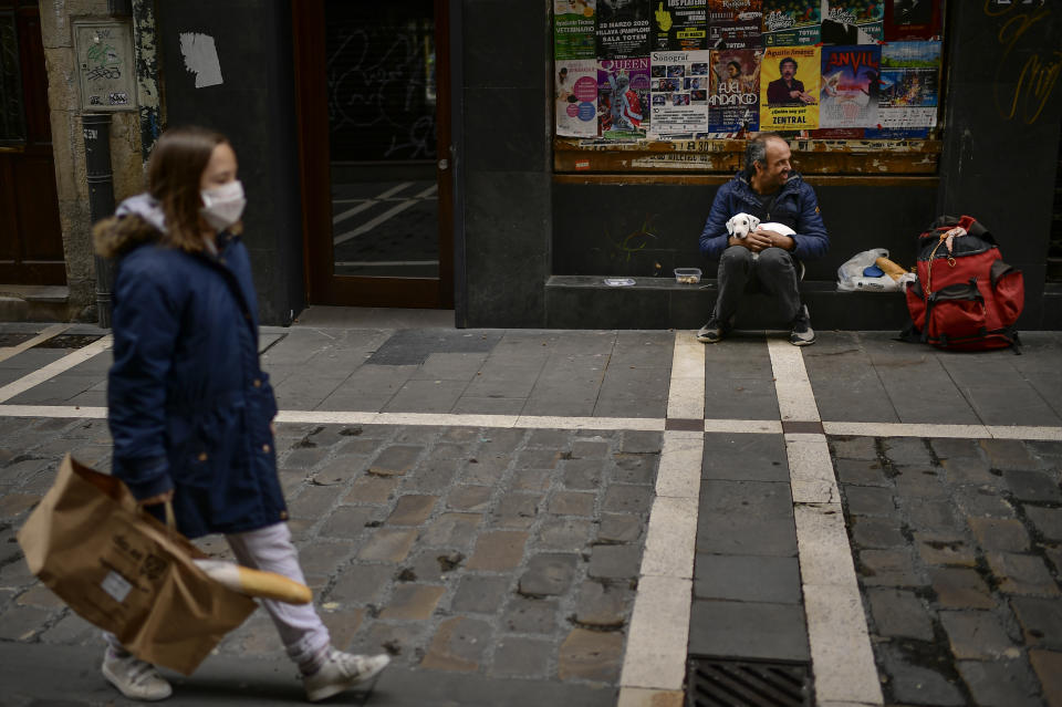 A woman wearing a face mask to prevent the spread of coronavirus during lockdown, walks past beside Vicente Mata, who is homeless, in Pamplona, northern Spain, Saturday, April 11, 2020. COVID-19 causes mild or moderate symptoms for most people, but for some, especially older adults and people with existing health problems, it can cause more severe illness or death. (AP Photo/Alvaro Barrientos)
