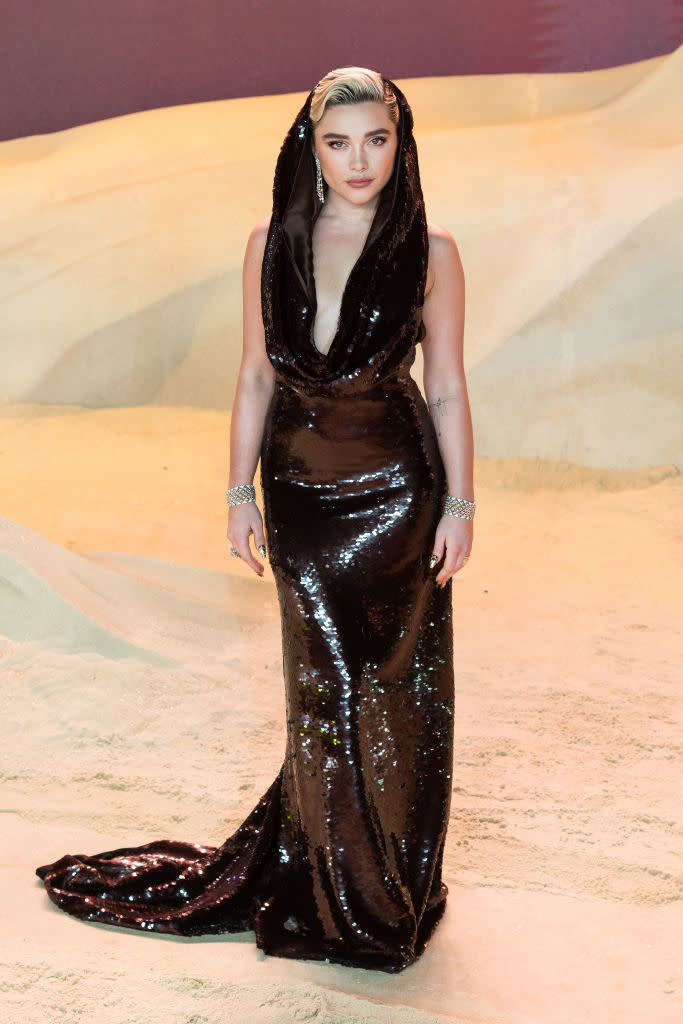 Person in a shiny, sleeveless floor-length gown with a deep neckline, accessorized with a headpiece and bracelet
