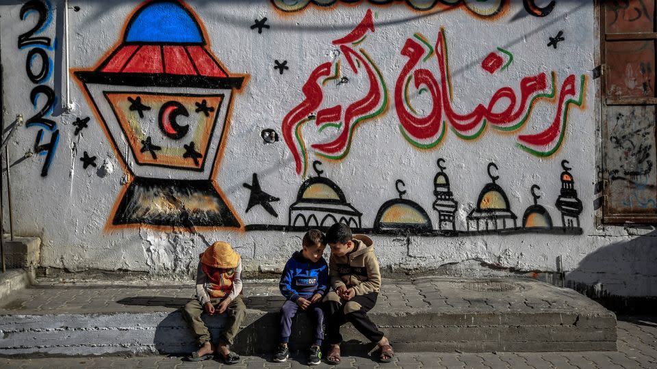 Palestinian children sit in front of Ramadan-themed mural in Gaza City on March 8. - AFP/Getty Images