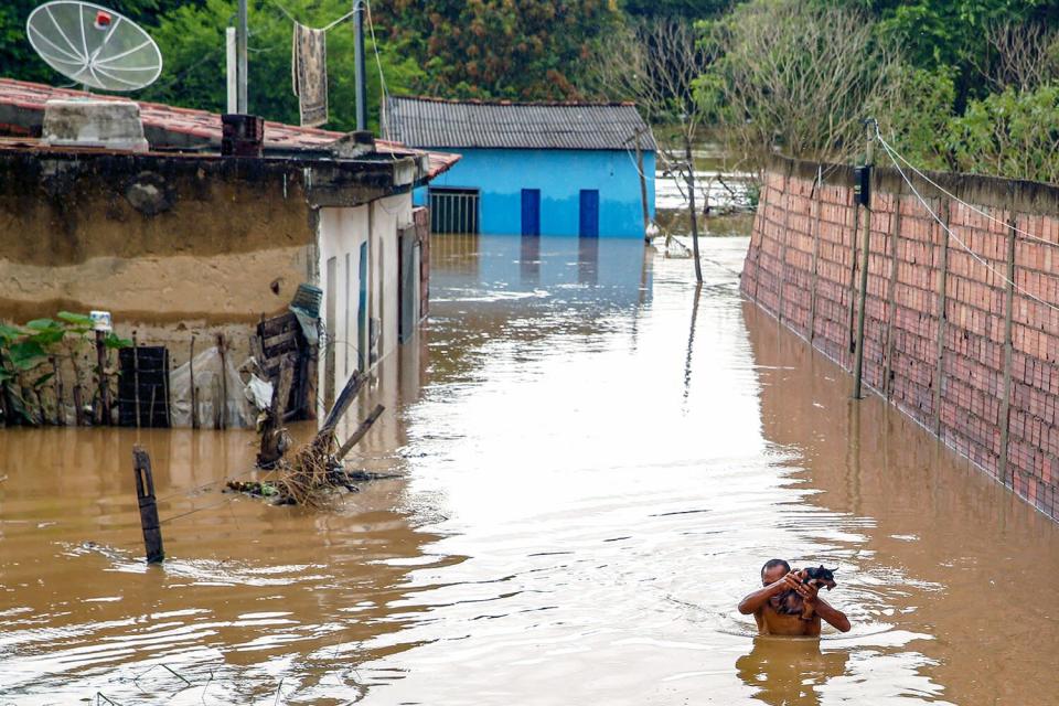 Em 26 de dezembro de 2022, um homem carregando um cachorro vagueia na água durante uma enchente causada por fortes chuvas em Idapettinga, Brasil, na província da Bahia.