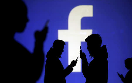 Silhouettes of mobile users are seen next to a screen projection of Facebook logo in this picture illustration taken March 28, 2018. REUTERS/Dado Ruvic/Illustration/Files