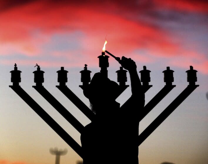 The sun sets behind Rabbi Tzviky Dubov of the Chabad of Greater Orlando as he lights the menorah, commemorating the first night of Hanukkah, during a ceremony at the Roth Jewish Community Center (JCC) in Maitland, Fla., Thursday, Dec. 10, 2020. (Joe Burbank/Orlando Sentinel via AP)