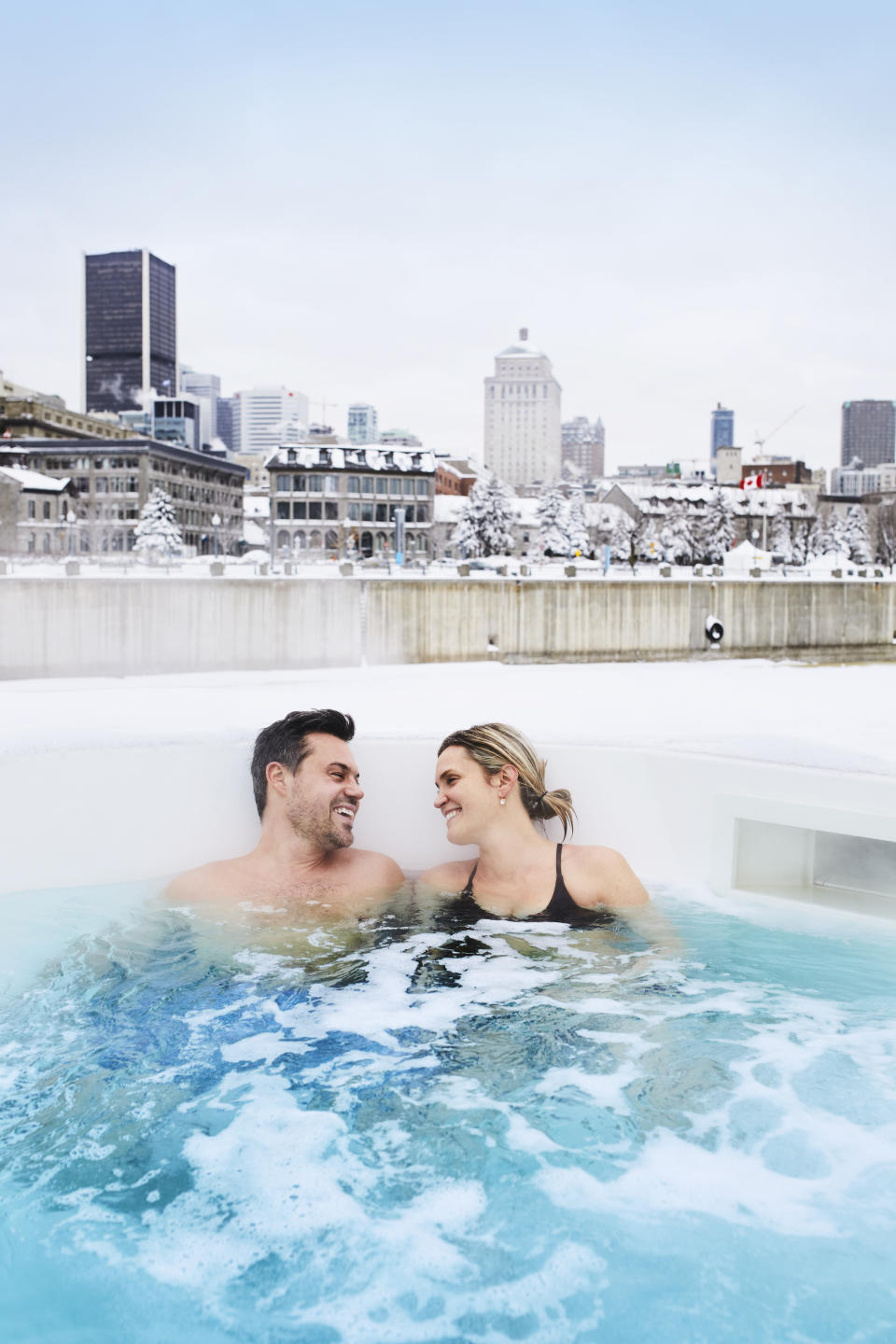 Happy couple enjoying the hot tub at Bota Bota spa in Old Montreal with a view of the skyline behind them