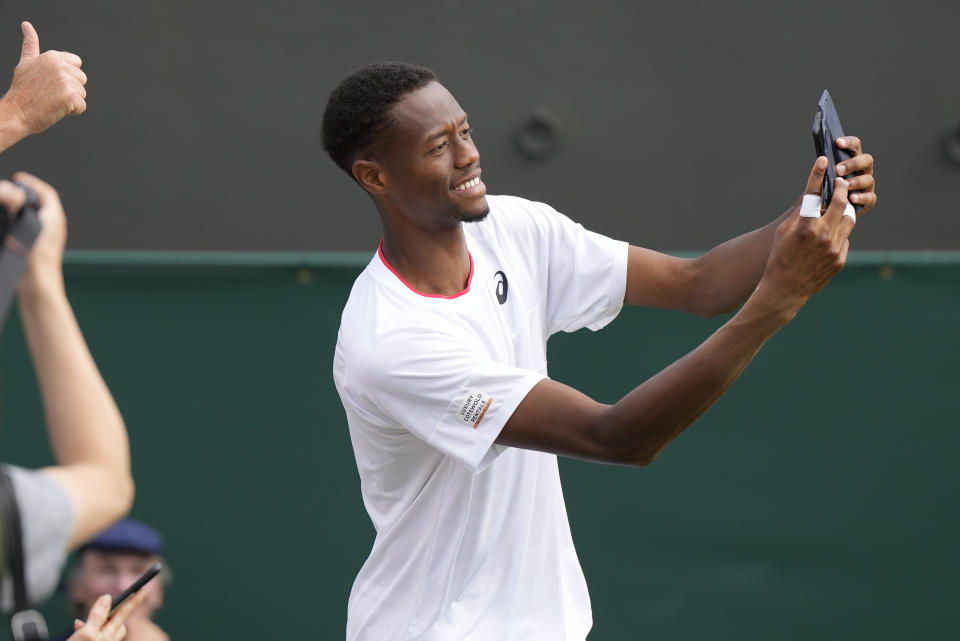 Christopher Eubanks of the US takes selfies with the crowd after beating Stefanos Tsitsipas of Greece in a men's singles match on day eight of the Wimbledon tennis championships in London, Monday, July 10, 2023. (AP Photo/Alastair Grant)