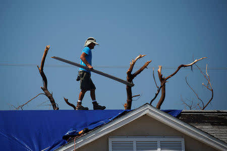 A roofer works on attaching a blue tarp to a roof following Hurricane Irma in Ramrod Key, Florida, U.S., September 18, 2017. REUTERS/Carlo Allegri