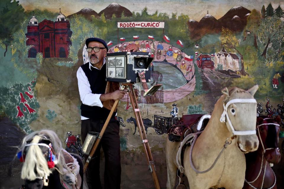 In this Sept. 2, 2016 photo, photographer Luis Maldonado poses for a portrait with his old wooden box camera as he waits for clients who want their portrait taken at a fair in Santiago, Chile. "I know that you have to eat and live. But if it were up to me, I'd only be doing box photos. It's what fills me up," he said. "I'd be empty without the box." (AP Photo/Esteban Felix)