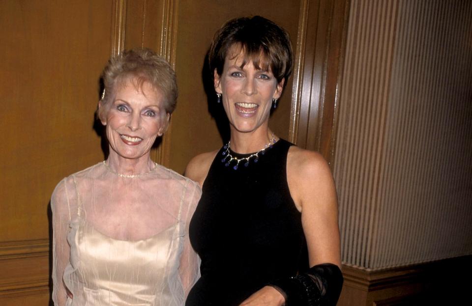 A woman in a sheer, white gown posing with a woman in a black gown