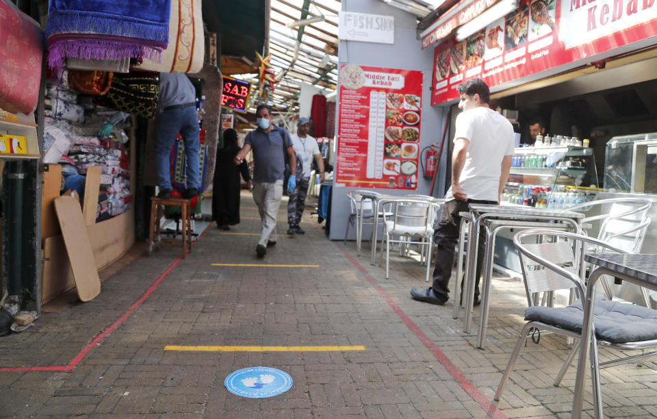 With social distancing markings in place on the pavement, as customers stroll through Shepherd's bush market that is allowed to reopen after the COVID-19 lockdown in London, Monday, June 1, 2020. The British government has lifted some restrictions to restart social life and activate the economy while still endeavouring to limit the spread of the highly contagious COVID-19 coronavirus. (AP Photo/Frank Augstein)