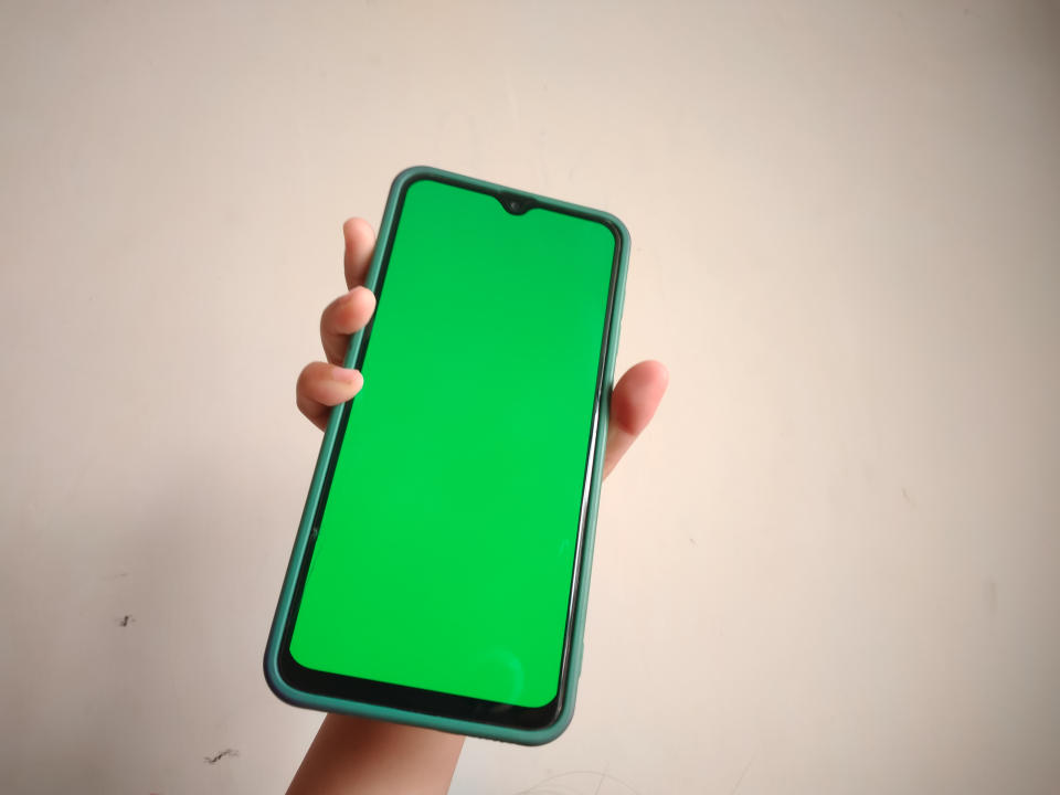 Child's hand holding a smartphone with green screen.