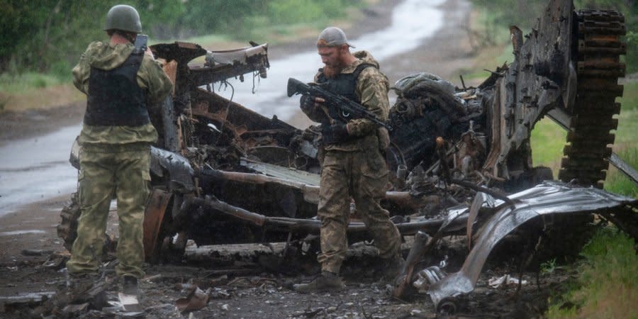 Ukrainian defenders pictured against the background of destroyed Russian military equipment