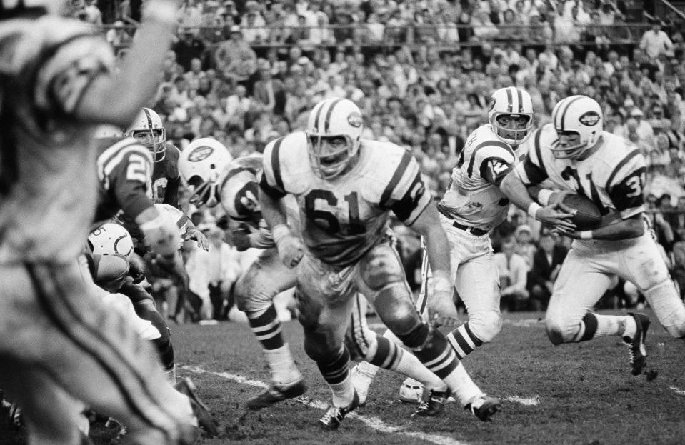 Keeping a watchful eye on a rushing defender, New York Jets quarterback Joe Namath hands off to running back Bill Mathis in Super Bowl III.