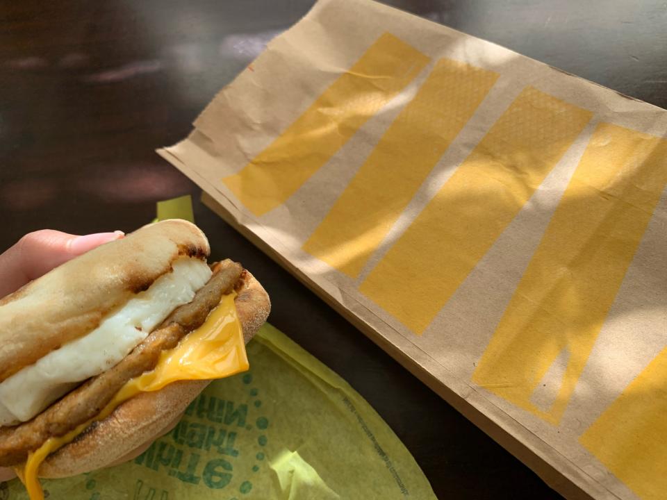 Handing holding a McDonald's McMuffin by yellow wrapper and brown bag