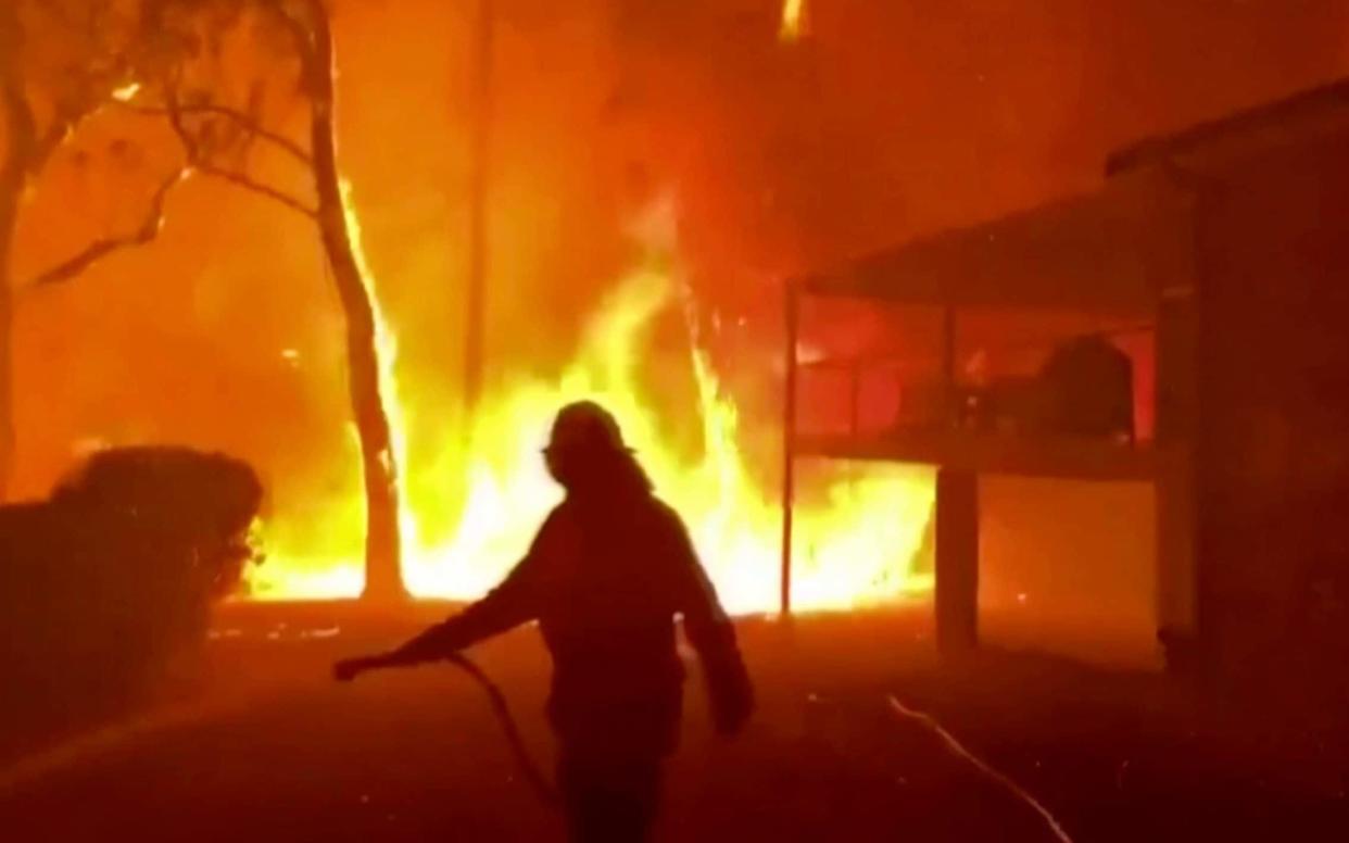 A firefighter sprays water on a blaze nearing a home in Blackheath, New South Wales, on December 22 - Twitter@NSWRFS