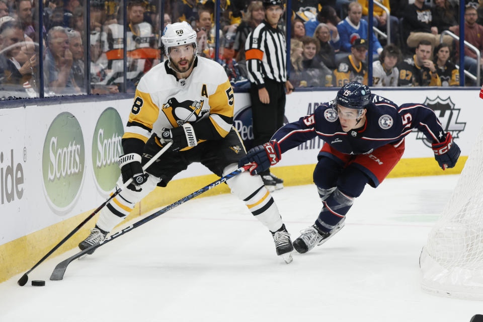 Pittsburgh Penguins' Kris Letang, left, looks to pass the puck as Columbus Blue Jackets' Gavin Bayreuther defends during the third period of an NHL hockey game Thursday, April 13, 2023, in Columbus, Ohio. (AP Photo/Jay LaPrete)