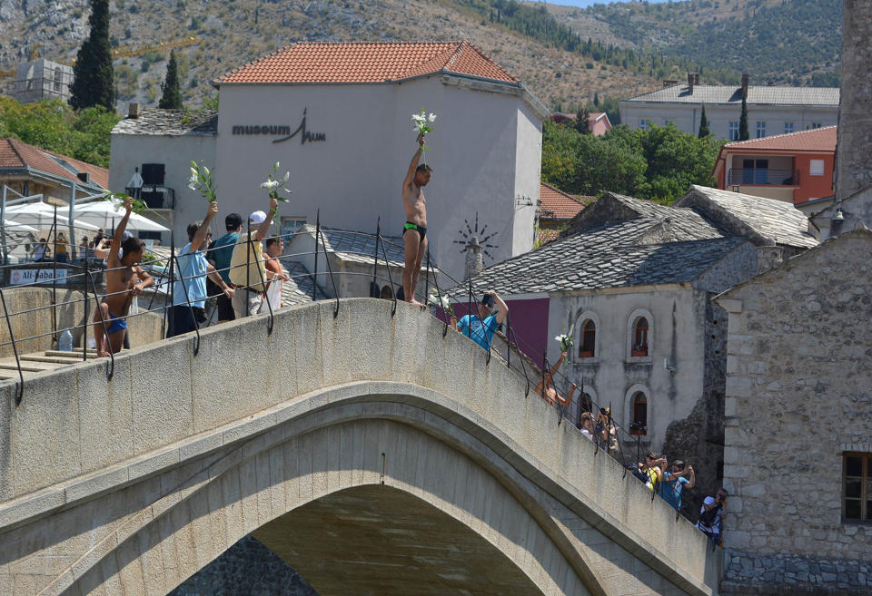 <p>A man holding flowers in his hand jumps into the Neretva river from historical “Old Bridge”, also known as “Mostar Bridge” to mark the 22nd anniversary of the 1995 Srebrenica genocide in Mostar, Bosnia and Herzegovina on July 11, 2017. (Photo: Zeljko Milicevic/Anadolu Agency/Getty Images) </p>