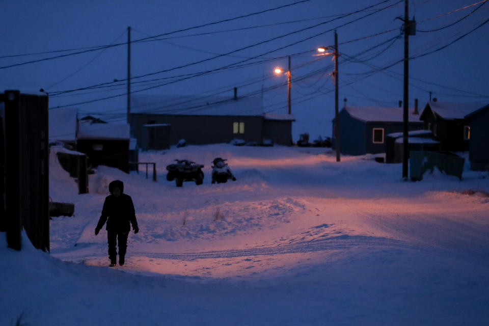 FILE - In this Jan. 20, 2020, file photo, a woman walks before dawn in Toksook Bay, Alaska, a mostly Yuip'ik village on the edge of the Bering Sea. Native American leaders are raising questions about how $8 billion in federal coronavirus relief tagged for tribes will be distributed, with some arguing that for-profit Alaska Native corporations shouldn't get a share of the funding. (AP Photo/Gregory Bull, File)