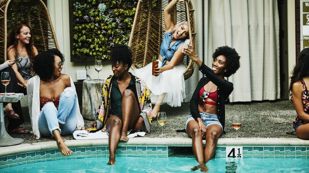 smiling woman sitting beside pool taking selfie with smart phone during party