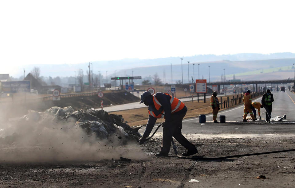 Police clear a smoking barricade on a road at Escort, in the KwaZulu-Natal Province, South Africa, Saturday, July 10, 2021 after trucks were set alight in overnight protests by supporters of former South African president Jacob Zuma who was imprisoned this week for contempt of court. The protesters are demanding that Zuma be released from prison immediately. (AP Photo)