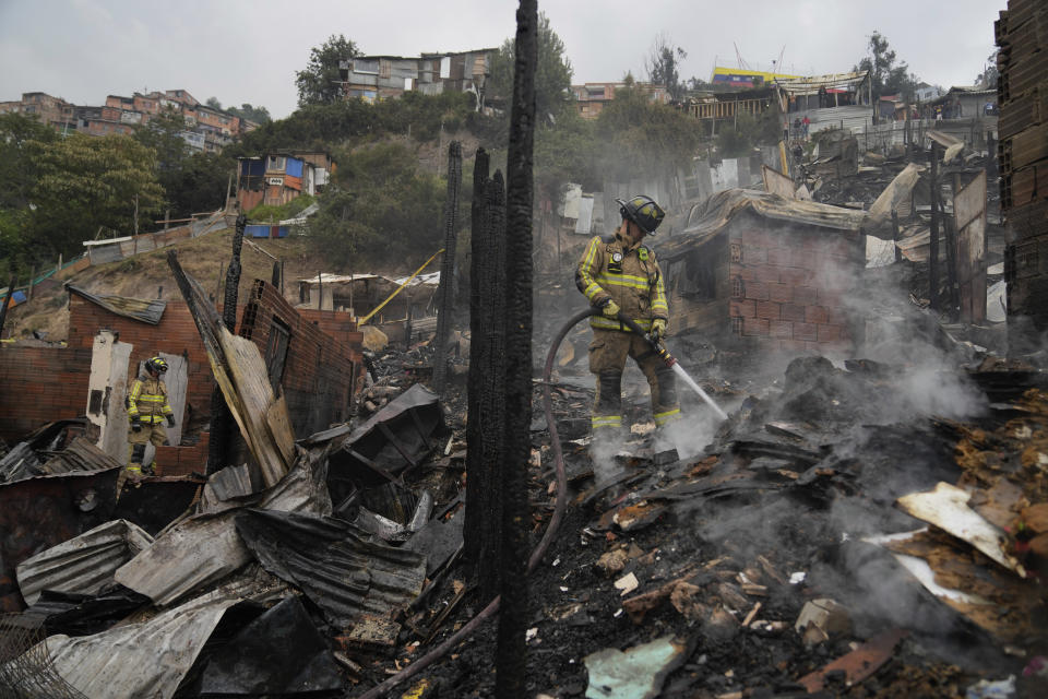 Los bomberos rocían agua sobre los escombros carbonizados de casas después de un incendio en Bogotá, Colombia, el viernes 8 de marzo de 2024. (AP Foto/Fernando Vergara)