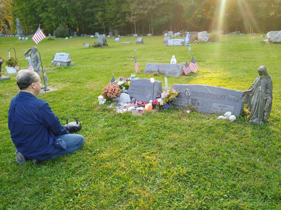 Beacon Journal history writer Mark J. Price listens to the Cars song "Moving in Stereo" at the headstones of Benjamin Orr and his brother and sister-in-law, Charles and Mary Orzechowski, at St. Patrick Cemetery in northern Geauga County.