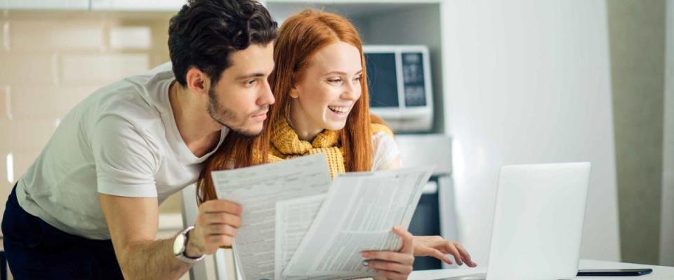 Happy couple at home paying bills with laptop and looking screen