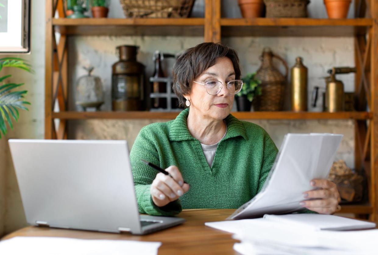 A mature woman during a document check. She checks the correctness of filling out the documentation and enters the data on the site. Modern technology in everyday life concept.