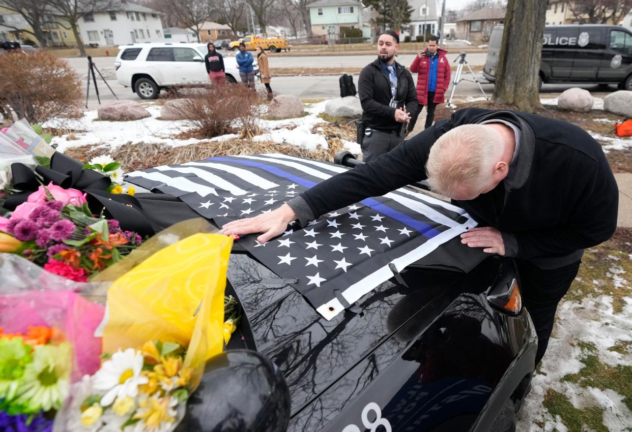 A Milwaukee Police detective places his hand on the hood of a Milwaukee squad car covered in flowers at Milwaukee Police Department District 4 on West Sliver Spring Drive to pay tribute to fallen officer Peter Jerving, who was shot and killed on Milwaukee’s south side on Tuesday, Feb. 7, 2023.